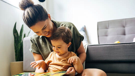 Mom reading a book with baby boy at home. Early age children education, development. Mother and child spending time together. Ca