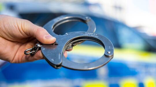 Handschellen vor Polizeiwagen - Symbolbild Handschellen vor Polizeiwagen - Symbolbild