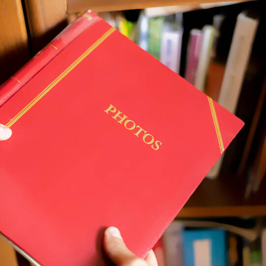 close up hand search and take the red photo album on the book shelf