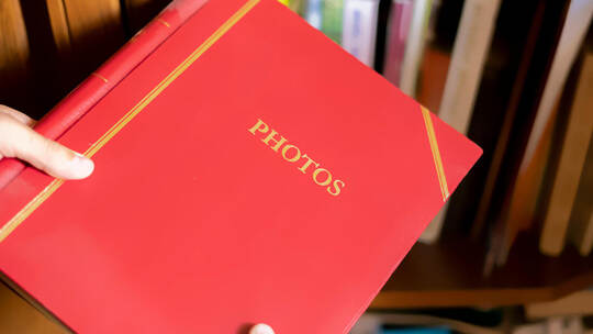 close up hand search and take the red photo album on the book shelf