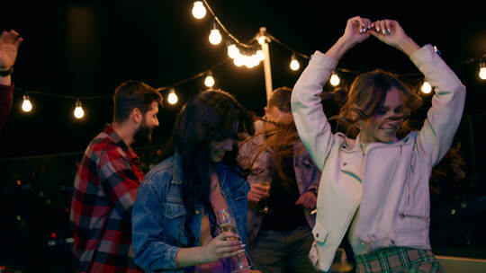 On the rooftop of terrace group of friends have fun time dancing and feeling happy at the party night time they drinking champag