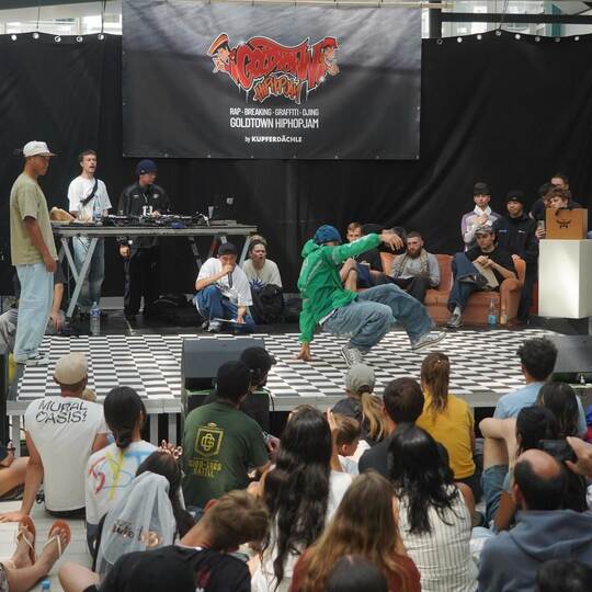 Auf einer großen Bühne duellieren sich die B-Boys und B-Girls im Breakdance. Die drei Judges entscheiden, wer die nächste Runde