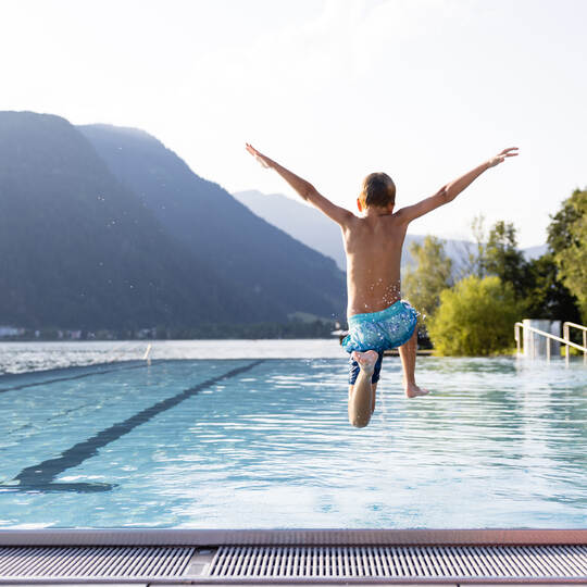 Active teenager boy jumping into an outdoor pool in the Alps. Summer holiday concept