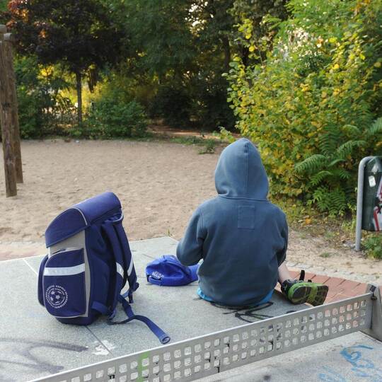Kind mit Schulranzen auf Spielplatz