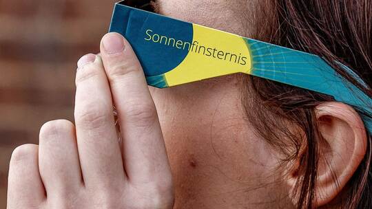 Frau mit Schutzbrille betrachtet eine partielle Sonnenfinsternis Frau mit Schutzbrille betrachtet eine partielle Sonnenfinsternis