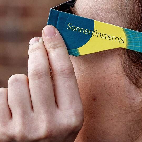 Frau mit Schutzbrille betrachtet eine partielle Sonnenfinsternis Frau mit Schutzbrille betrachtet eine partielle Sonnenfinsternis