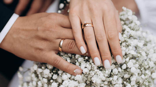 Newly wed couple's hands with wedding rings on a bouquet.