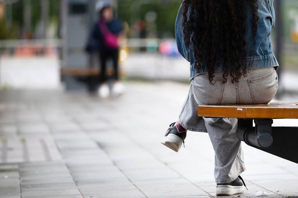 Eine junge Frau sitzt an einer Haltestelle auf einer Bank Eine junge Frau sitzt an einer Haltestelle auf einer Bank
