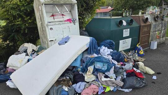 Ein Kleiderberg samt Matratze türmt sich vor dem Sammelcontainer. Die alten Materialien liegen auch bis unter die Bäume. Foto: M