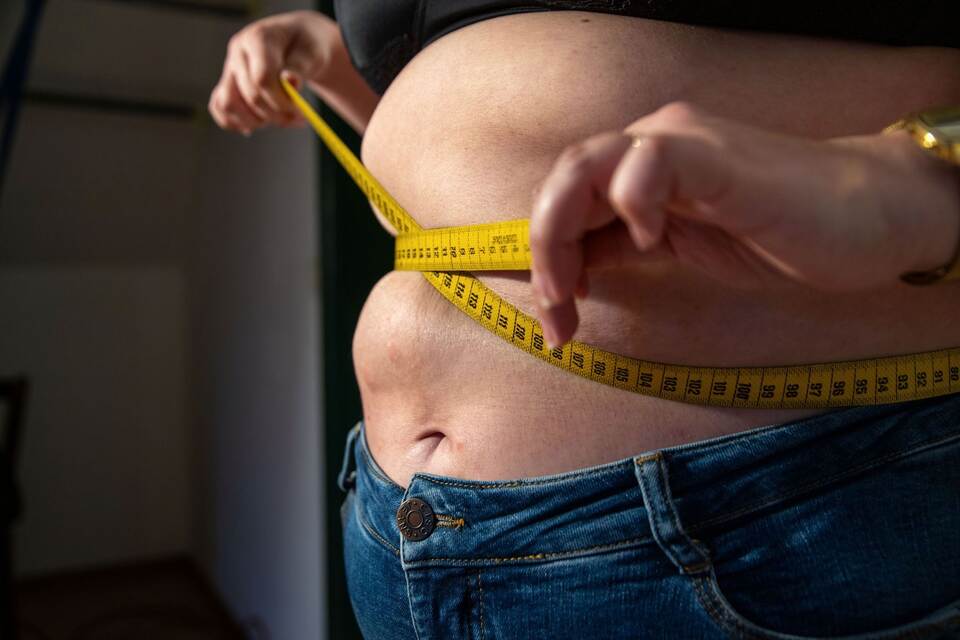 Eine Frau mit Übergewicht hält ein Maßband um ihren Bauch. Eine Frau mit Übergewicht hält ein Maßband um ihren Bauch.