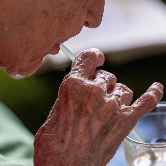 Eine Seniorin trinkt mithilfe eines Strohhalms