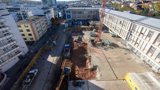 Blick von oben: Bagger und Lastwagen tragen die letzten Reste Fundament ab. Zurück bleibt ein großes Erdloch auf dem Parkplatz d