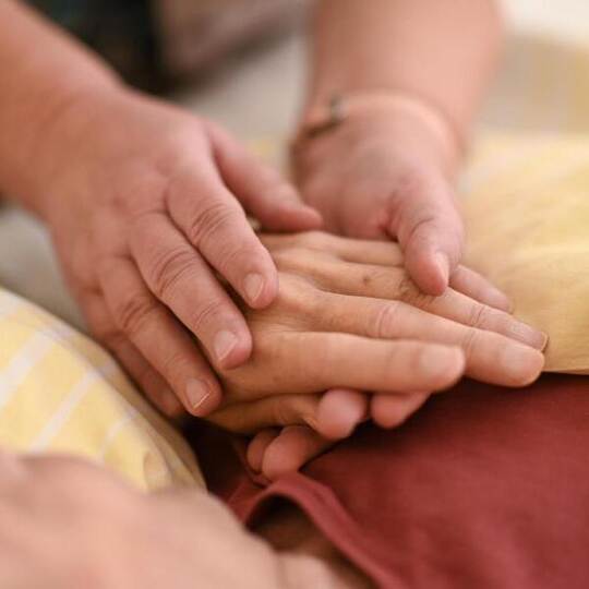 Eine Hospizmitarbeiterin hält die Hand eines todkranken Menschen, der im Hospiz im Bett liegt. Foto: Felix Kästle/dpa Eine Hospizmitarbeiterin hält die Hand eines todkranken Menschen, der im Hospiz im Bett liegt. Foto: Felix Kästle/dpa