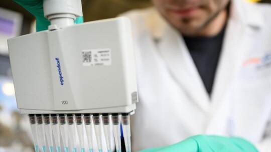 Ein Mann pipettiert in einem Labor des biopharmazeutischen Unternehmens Curevac eine blaue Flüssigkeit. Foto: Sebastian