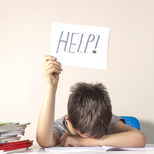 Sad tired frustrated boy sitting at the table with many books and holding paper with word Help. Learning difficulties, education