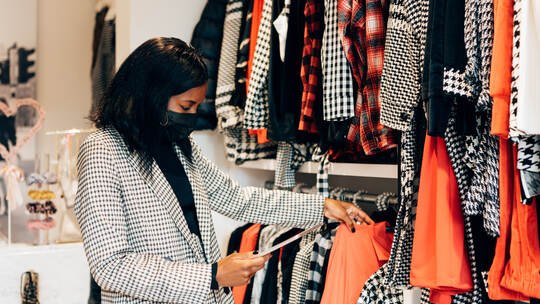 black woman manager in a fashion retail store is wearing a mask as protection against virus and using a tablet for working and c