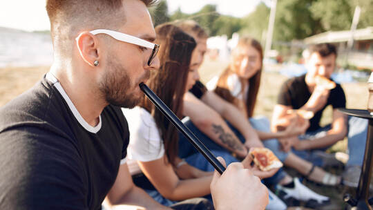 Young people eating pizza smoking shisha outside