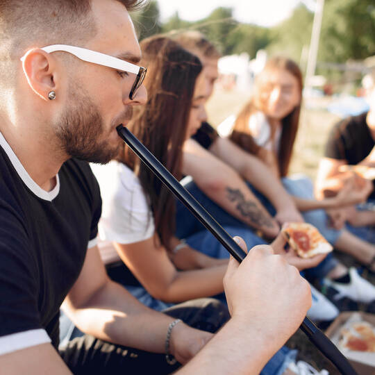 Young people eating pizza smoking shisha outside
