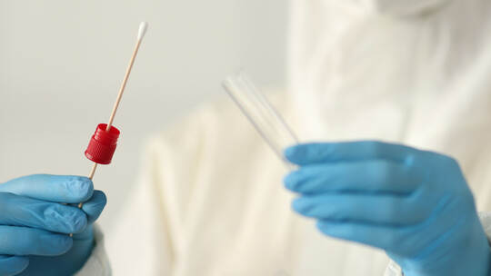 Doctor in protective suit holding test tube and cotton swab in clinic