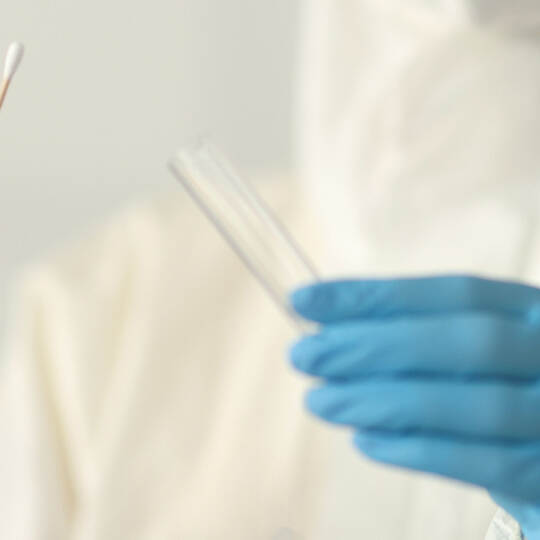 Doctor in protective suit holding test tube and cotton swab in clinic