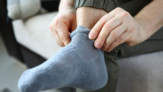Man at home in morning puts gray socks on his leg