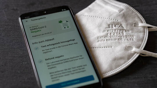 BERLIN, GERMANY - Mar 13, 2021: Corona Warn App shows a negative covid test result on a mobile phone next to a ffp2 respirator m