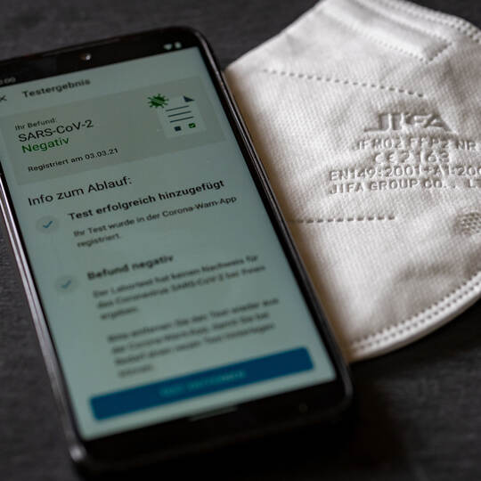BERLIN, GERMANY - Mar 13, 2021: Corona Warn App shows a negative covid test result on a mobile phone next to a ffp2 respirator m