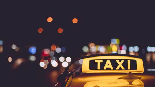 Yellow and black sign of a taxi put on a car at night