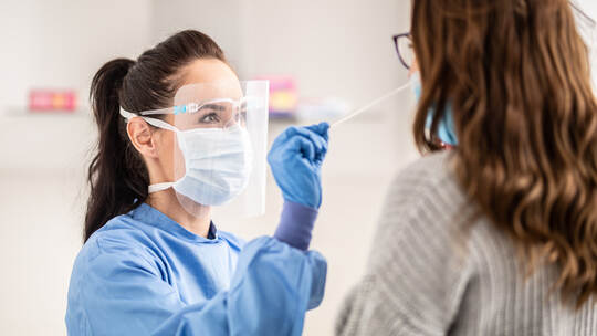 Female medical staff worker wearing protective equipment takes sample from nose of a patient to antigen test for coronavirus.