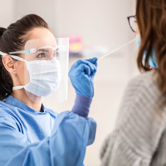 Female medical staff worker wearing protective equipment takes sample from nose of a patient to antigen test for coronavirus.