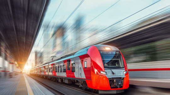 Electric passenger train drives at high speed among urban landscape.
