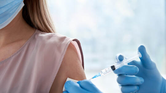 Male doctor making covid 19 vaccination injection in shoulder of female patient.