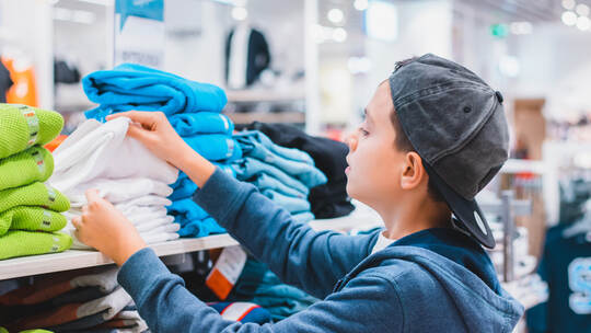A boy choosing and picking right clothes in the store. Shopping and sales concept. Black friday and holidays discount idea.