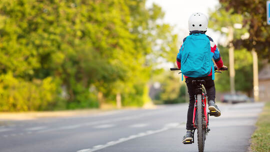 Child with rucksack riding on bike in the park near school