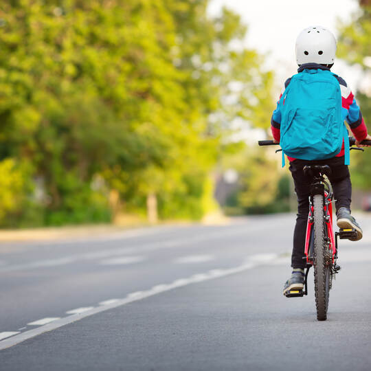 Child with rucksack riding on bike in the park near school