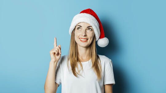 Young woman in Santa Claus hat with a mysterious face on a blue background. Concept idea for new year and christmas