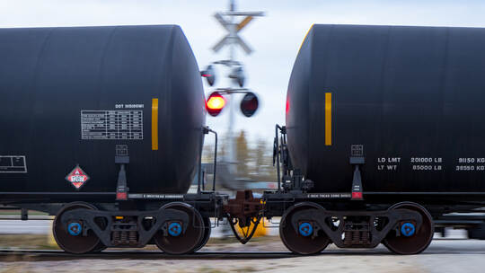 Tank Cars Connected Together Passing a Flashing Railway Crossing
