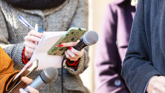 News reporter or TV journalist at press conference, holding microphone and writing notes