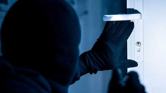 Robber in black balaclava cracking door with metal picklock