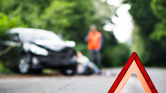 A close up of a red emergency triangle on the road in front of a car after an accident.