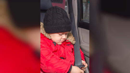 Transportation of small children in the car. A boy in a red jacket sits in a car that is not equipped with a child restraint and