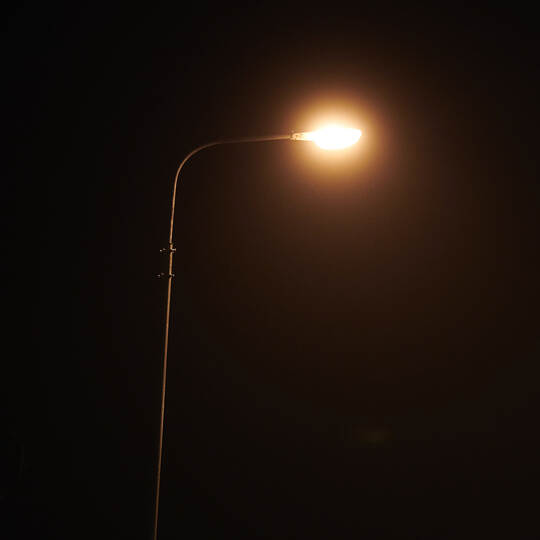 One night lamppost shines with faint mysterious yellow light through evening fog, copy space