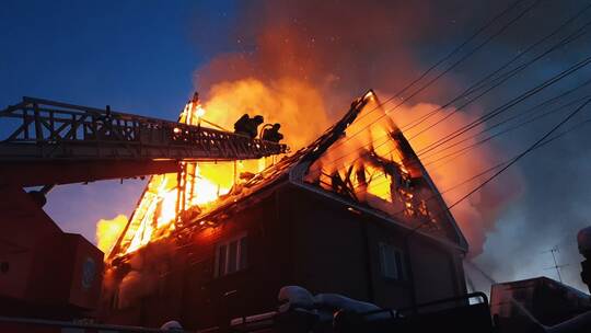 The roof of the house is on fire. The residential building burn, village. Firefighters put out a fire from the crane from above.