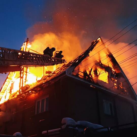 The roof of the house is on fire. The residential building burn, village. Firefighters put out a fire from the crane from above.