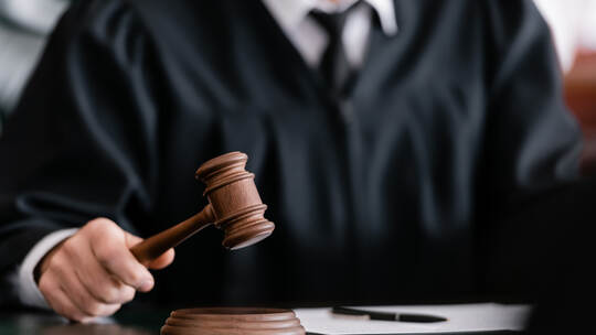 partial view of blurred judge in robe holding gavel in court