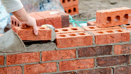 Hard working bricklayer lays bricks on cement mix on construction site. Fight housing crisis by building more affordable houses