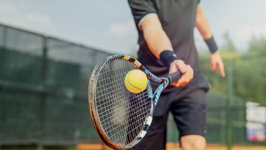 Close up of man playing tennis and beating the ball with a racket.