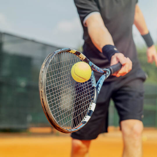 Close up of man playing tennis and beating the ball with a racket.