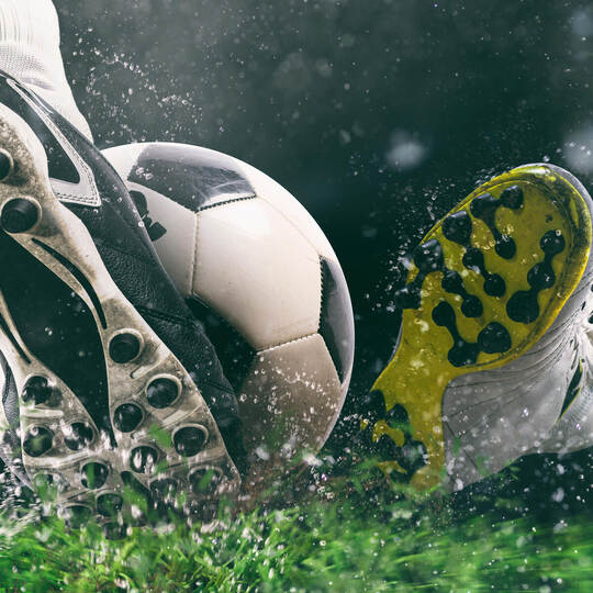 Football scene at night match with close up of a soccer shoe hitting the ball with power