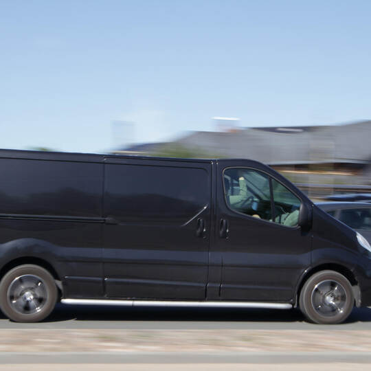 A black van is driving down the street at high speed. Motion blur